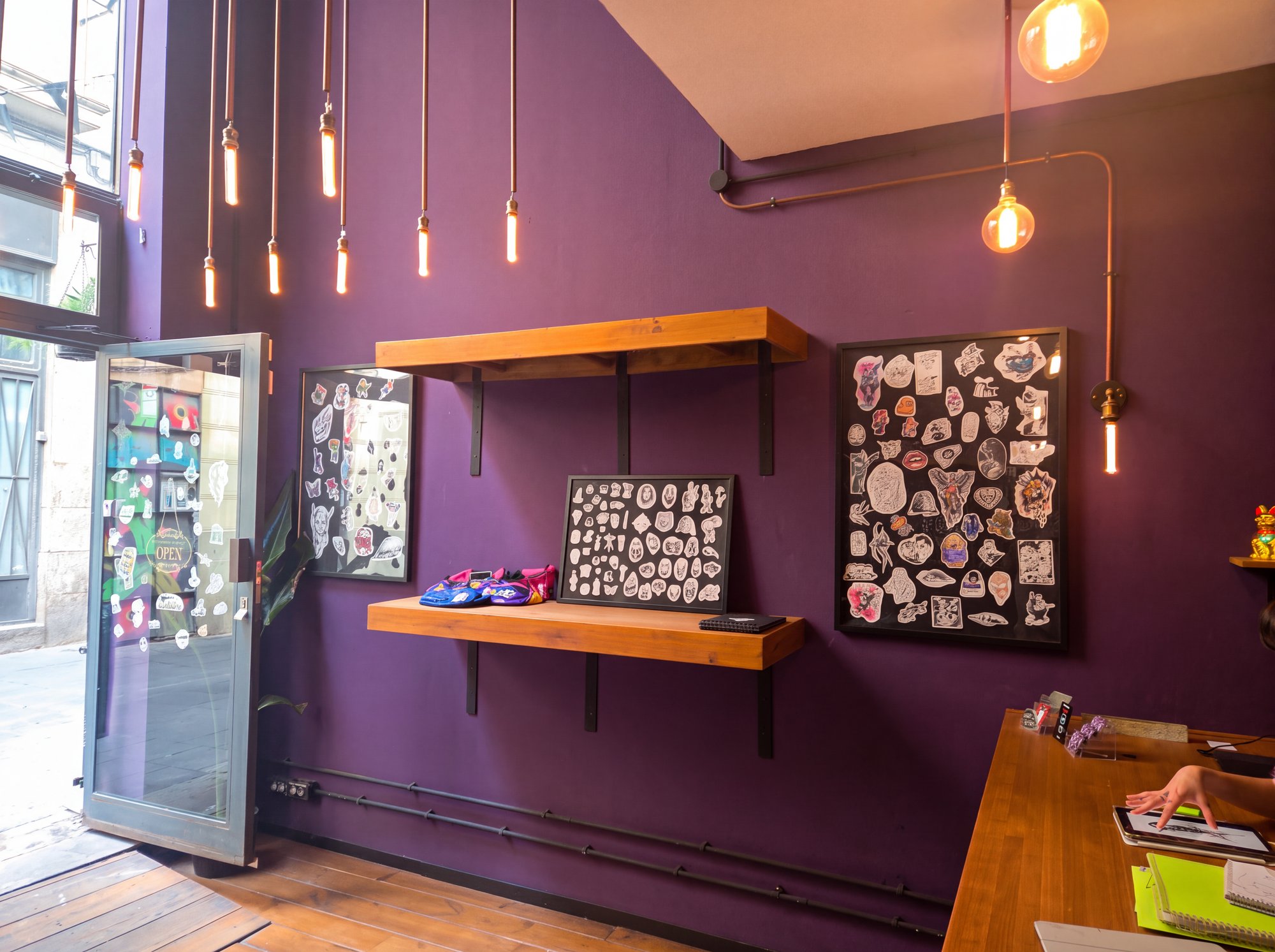 La sala de Nox Tattoo, pared morada, bombillas colgantes y láminas de flash enmarcadas